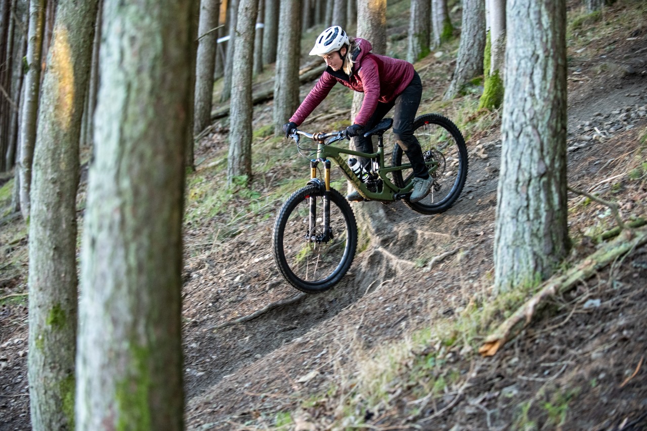 Woman riding mountain bike on technical descent through forest in Scotland