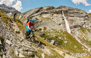 Two mountain bikers riding past a waterfall in a high alpine area