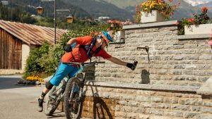 Mountain biker refilling water bottle at a water fountain surrounded by flowers