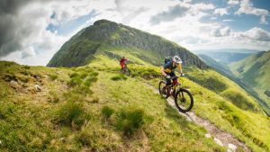 Rab Wardell and Pete Scullion ride along a singletrack with mountains in the distance
