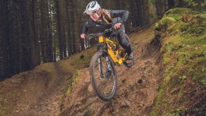 woman mountain bike rider descending steep technical trail on yellow bike