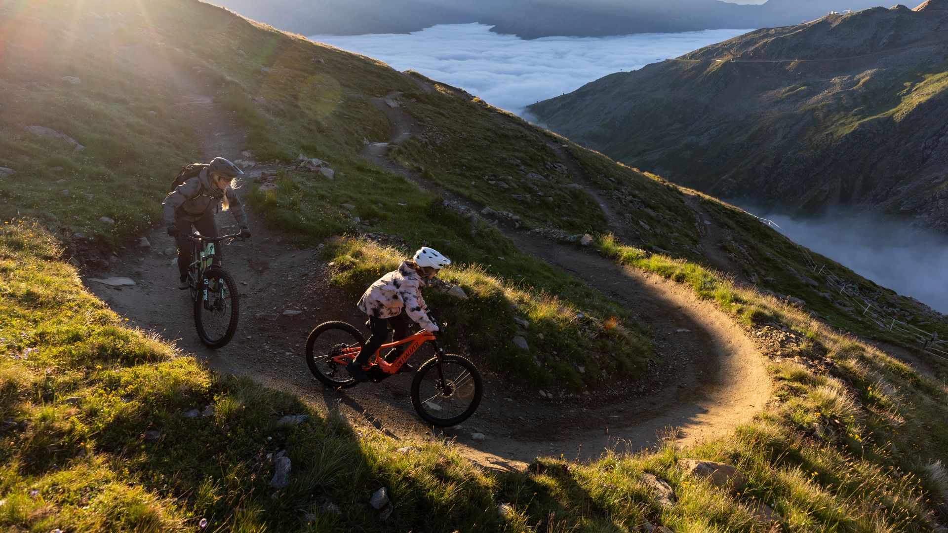 Girl riding down a mountain trail on the Specialized Levo SL Kids 2023 eMTB e-bike followed by her mother