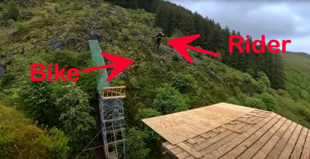 Still from YouTube video of mountain biker jumping across canyon in Wales and crashing