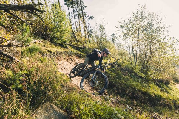 Mountain biker on a YT Jeffsy turning a corner on a wide sunny hillside