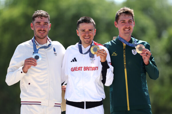 Tom Pidcock holds his gold medal on the podium, sorounded by Silver medalist Victor Koretzky on the left and Bronze medalist Alan Hatherly on the right