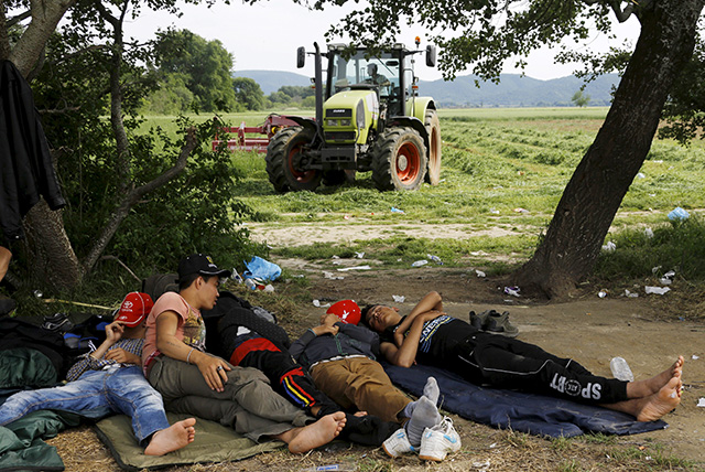 A Greek farmer drives his tractor as Afghan immigrants sleep on the Greek-Macedonian border before an attempt to flee to Macedonia from the border village of Idomeni in Kilkis prefecture May 13, 2015. Hundreds of mostly Afghan, Syrian, and African immigrants cross daily from Greece into Macedonia on their way to northern European countries; most of them are turned back by Macedonian border guards. REUTERS/Yannis Behrakis - RTX1CUK2