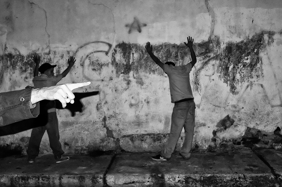 An officer points his finger as a capture signal of another individual during a night patrol in one of the slums in the city of Merida/Venezuela.