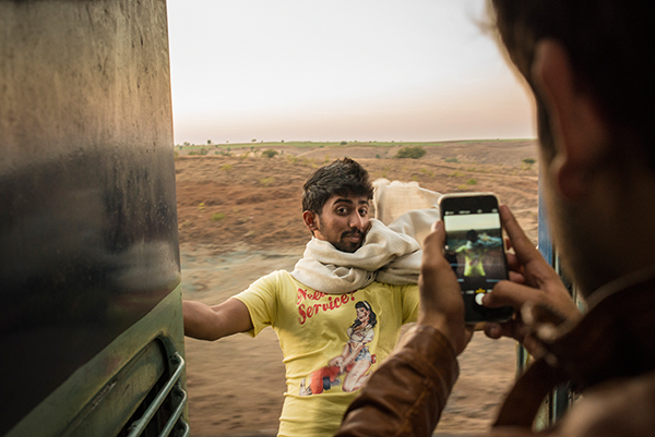 A young man leans out of a moving train while his friend takes a picture