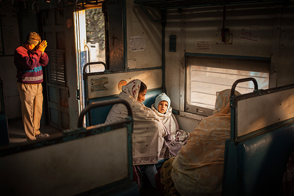 Two women and a child wrapped up against the morning cold, while behind them a man offers a prayer to the sun