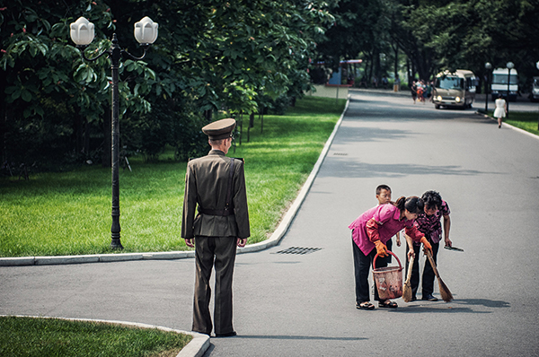 Street sweepers keep Pyongyang’s streets clean under the watchful eye of a solider