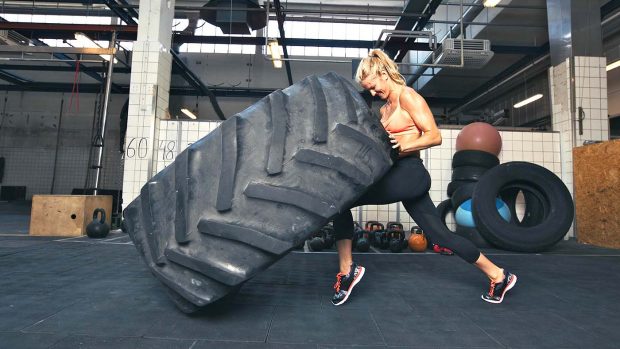 E4RRGN Fit female athlete working out with a huge tire, turning and flipping in the gym. Crossfit woman exercising with big tire.