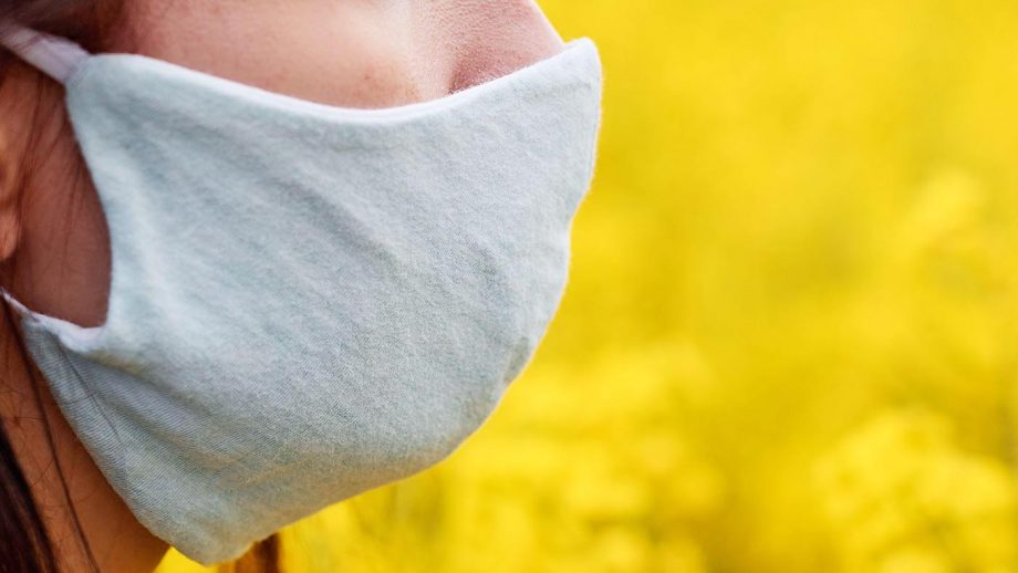 2BKC185 Close up womans face in a protective mask on the yellow rape flowers background. Healthcare concept against coronavirus or allergy.