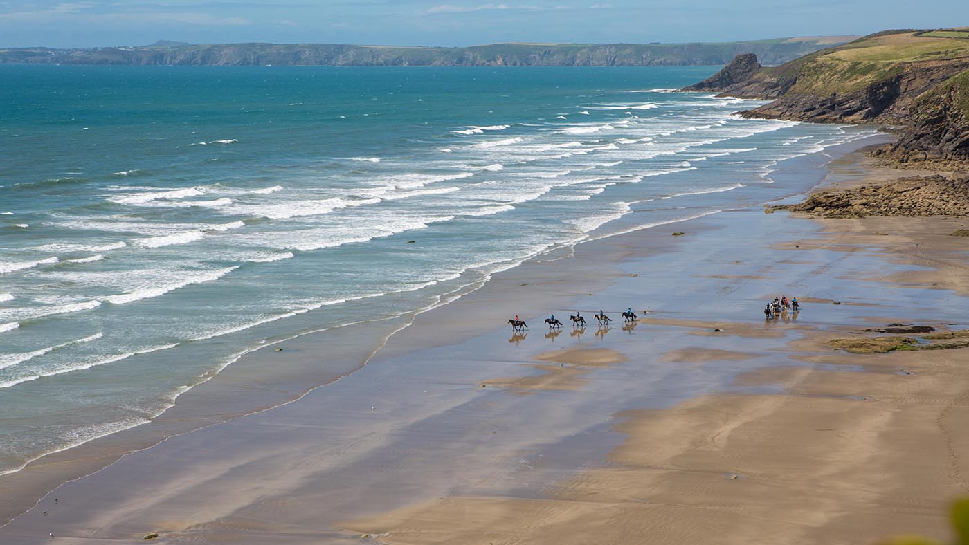 2A847AF Looking down at a group of horse riders riding on an empty beach in Pembrokeshire, Wales.