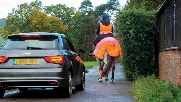 A car driving close behind a horse and rider who are wearing high-vis