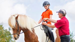 Instructor teaching young girl how to ride a horse and hold the reins