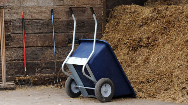 Large blue wheelbarrow upturned at a muckheap on a horse yard