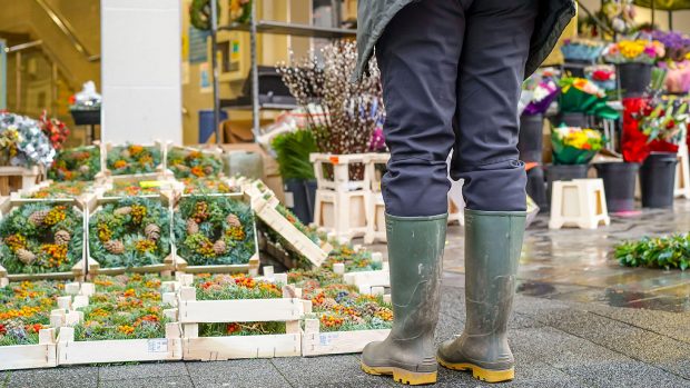 2DFHNC6 Kidderminster, UK. 5th December, 2020. The first Christmas shopping weekend after Lockdown Two restrictions are lifted sees early morning market traders setting up their stalls for what they hope will be a busy festive trading day. With shoppers expected to be out in force, public warning signs are in place around the town reminding folk about essential social distancing measures. A woman (lower section) wearing wellies stops to look at Yuletide wreaths for sale. Credit: Lee Hudson/Alamy Live News