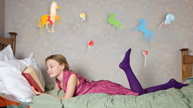 Young girl reading a book on her bed, with horse decorations on the wall behind her