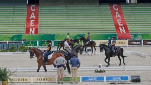 A group of international riders in a warm-up arena.