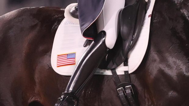 An American dressage rider's leg showing shiny black boot tail coat and the American flag on a white saddle cloth