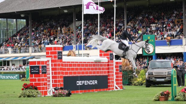 Showjumper Joe Truckfield and grey gelding Crisue clear the big red puissance wall in front on the packed grandstand at Dublin Horse Show 2024.