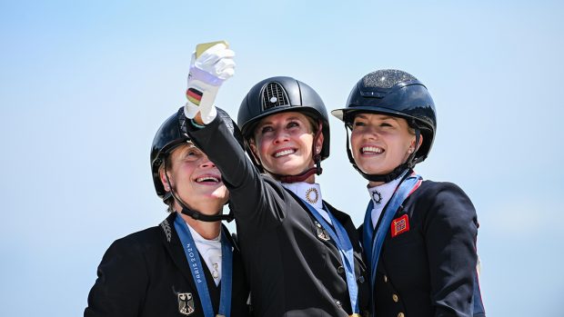 Jessica von Bredow-Werndl takes a selfie on the olympic podium with her fellow medal winners Isabell Wearth and Lottie Fry