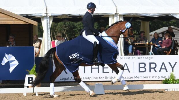 Jezz Palmer and Premier, a bay horse, pictured cantering around their lap of honour wearing a blue rug and rosette at the Lemieux National Dressage Championships 2024