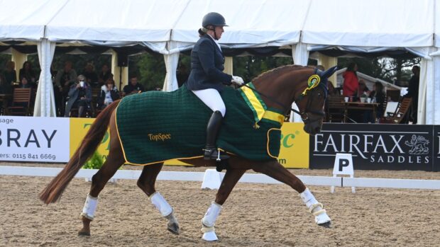 Elementary silver winner in the lap of honour. Woman riding a chestnut mare wearing a green rug.