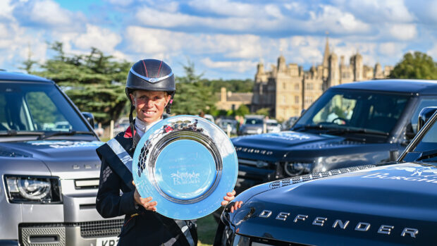 Ros Canter holds the Defender Burghley trophy flanked by Defender vehicles in front of Burghley House