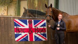 Becky Moody stands beside Jaegerbomb in front of one of their flags from Paris which adorns their indoor school.