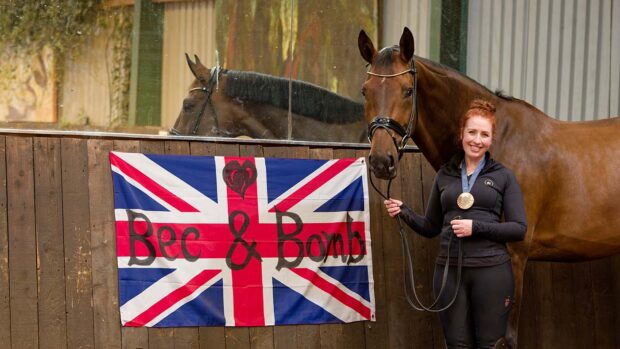 Becky Moody stands beside Jaegerbomb in front of one of their flags from Paris which adorns their indoor school.