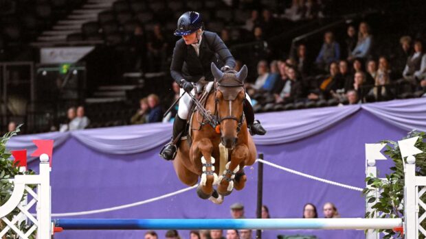 Michaela Scott and Eddie G Z jump a fence towards the camera with the iconic HOYS purple area boards behind them on their way to winning the 2024 Foxhunter title.