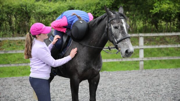 Woman riding a dark grey horse leaning on his neck crying. Another woman on the ground comforts her.