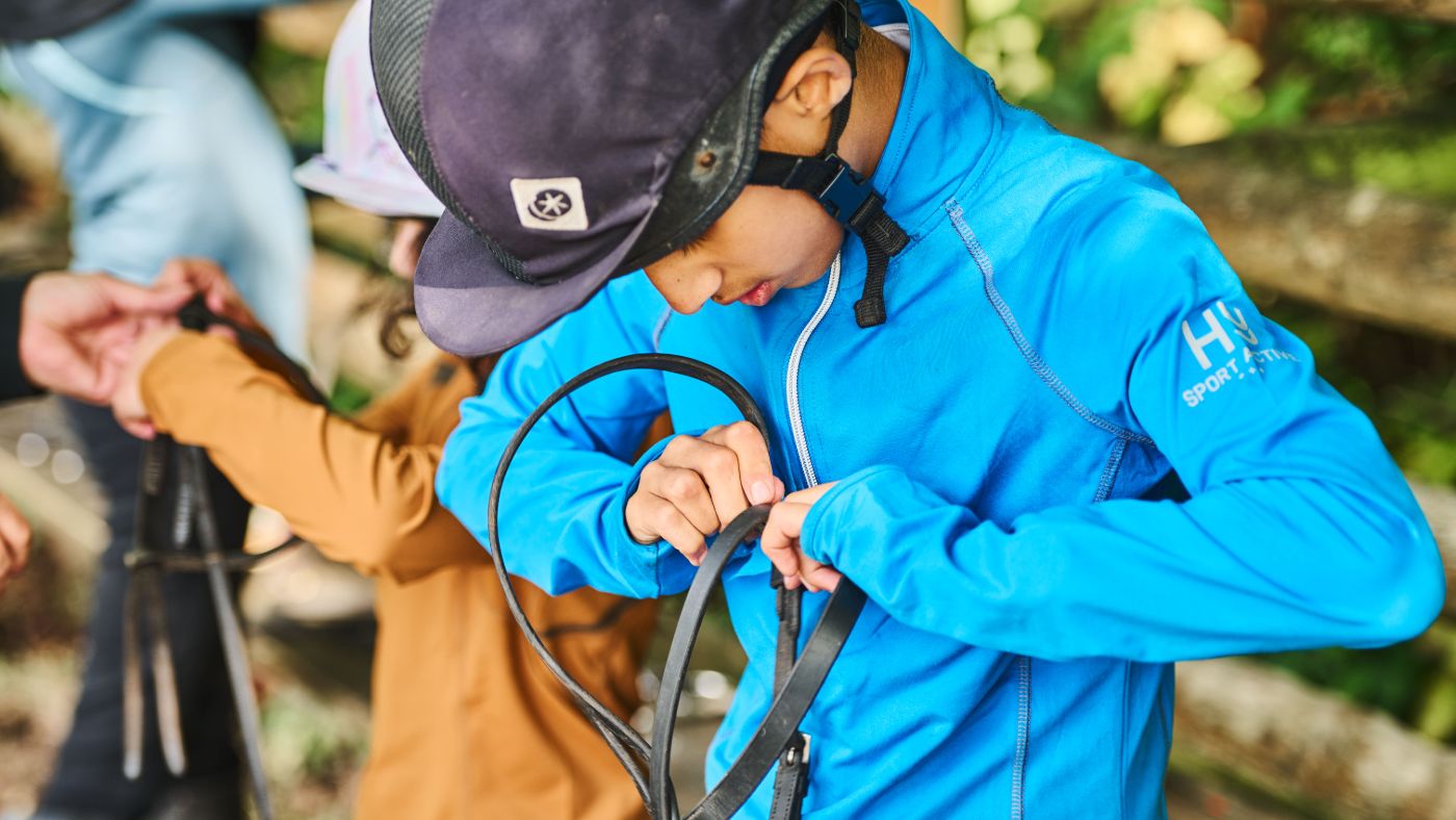 Boy in a blue top taking apart a bridle