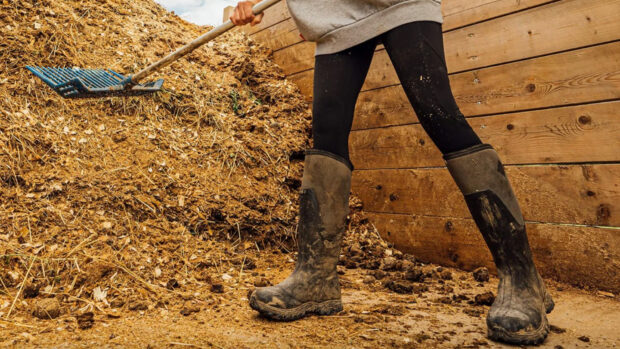 Horse owner wearing a pair of the best neoprene wellies while tidying a muckheap