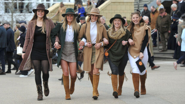 Five ladies walking arm-in-arm dressed up for Cheltenham races