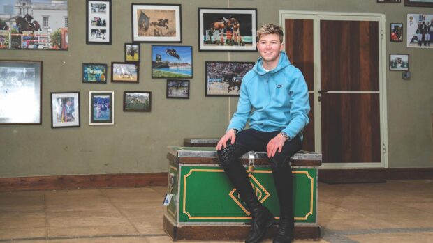 Harry Charles sitting on a trunk at home in front of a wall of pictures of his competing.