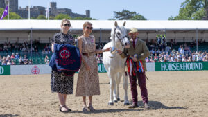 Horse & Hound’s Nicola McClure and Martha Terry present Connemara stallion Clover Hill Magic, handled by Jamie Frost, with a cup for winning the Horse & Hound Mountain and Moreland Supreme In Hand Championship at Royal Windsor Horse Show with the Windsor Castle behind the spectator stands.