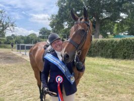Victoria Bertorelli stands next to An Cathaoir, a one-eyed ex-racehorse fr a photo with their rosette and sash after winning the amateur RoR championship at Hickstead.