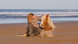 Emma Massingale sitting with a pony on a beach: introduction to liberty training