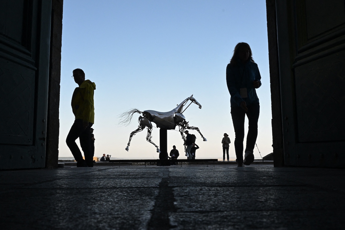 Guests and journalists stand next to Zeus, the mechanical horse used in the Paris 2024 Olympic Games' opening ceremony, after it was installed for display on the terrace of the abbey of Mont Saint-Michel on July 9, 2025. The emblematic horse will be on display until September 7, 2025. (Photo by Damien MEYER / AFP)