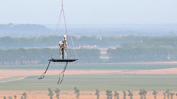 A helicopter transports Zeus, the mechanical horse used in the Paris 2024 Olympic Games' opening ceremony, to be installed for display on the terrace of the abbey of Mont Saint-Michel on July 9, 2025. The emblematic horse will be on display until September 7, 2025. (Photo by Damien MEYER / AFP)