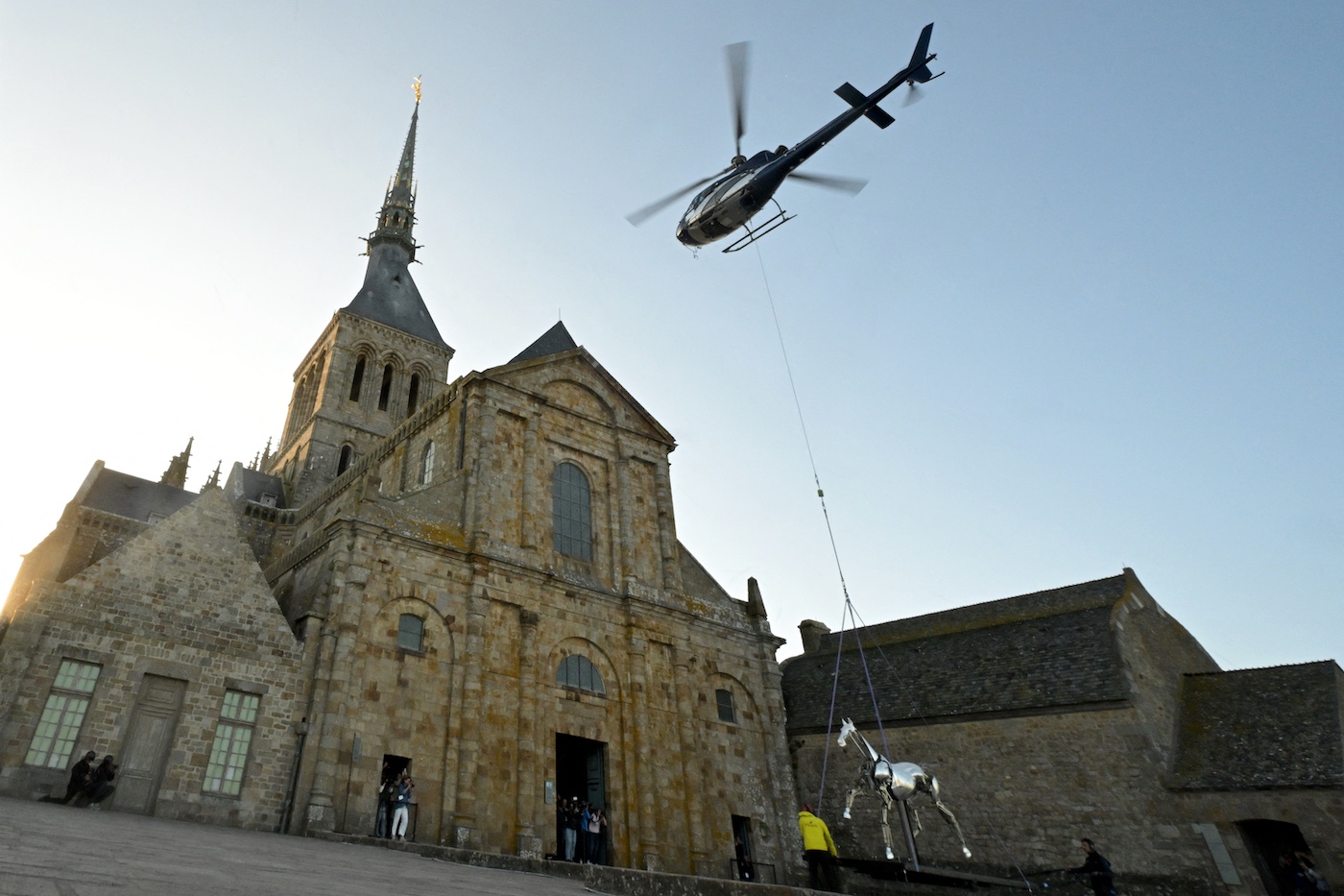 A helicopter drops off Zeus, the mechanical horse used in the Paris 2024 Olympic Games' opening ceremony, to be installed for display on the terrace of the abbey of Mont Saint-Michel on July 9, 2025. The emblematic horse will be on display until September 7, 2025. (Photo by Damien MEYER / AFP)