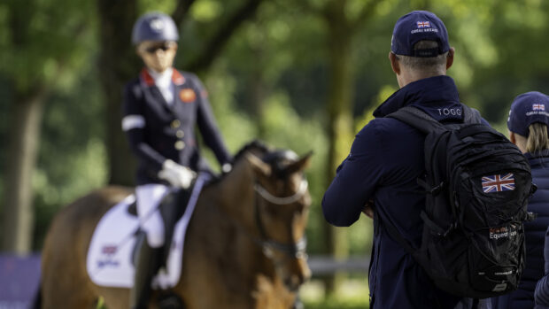A trainer pictured from behind with a para dressage rider in soft focus in the background