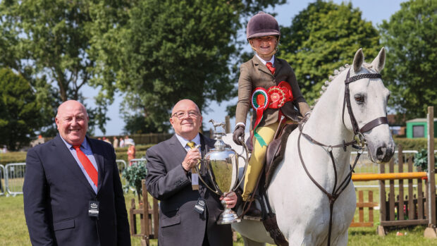 Nigel and Stuart Hollings stand alongside a grey working hunter pony holding a large trophy.