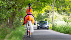 View of horse and rider on road wearing full hi-vis, with car approaching