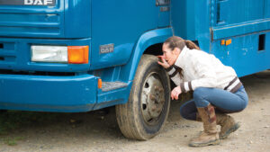 Owner of horsebox inspecting wheels and tyres as part of preparing horse kit for winter