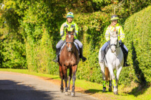 Two horse riders wearing hi-vis jackets and hat bands. One horse wearing hi-vis leg wraps.