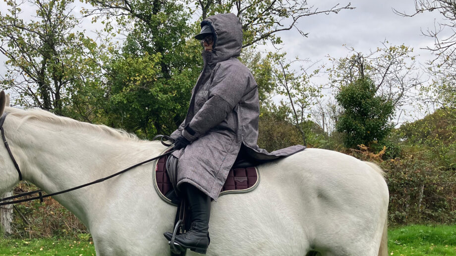 Lady wearing Hestt Eco-Ultra Riding Robe with hood up on horse side view