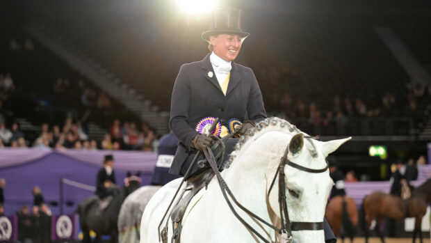 A winning side saddle rider wearing a veil and top hat on board a grey hunter with the spotlight behind her in the main arena at HOYS 2025.